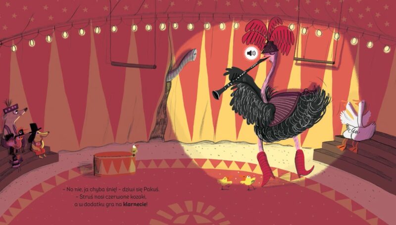 Książka dźwiękowa „Pakuś i orkiestra cyrkowa” – arena cyrkowa, ubrany w czerwone kozaki ogromny struś gra na klarnecie, reszta zwierząt siedzi zasłuchana